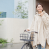 雨の日の玄関でベージュのレインポンチョを着て自転車のそばに立つ女性