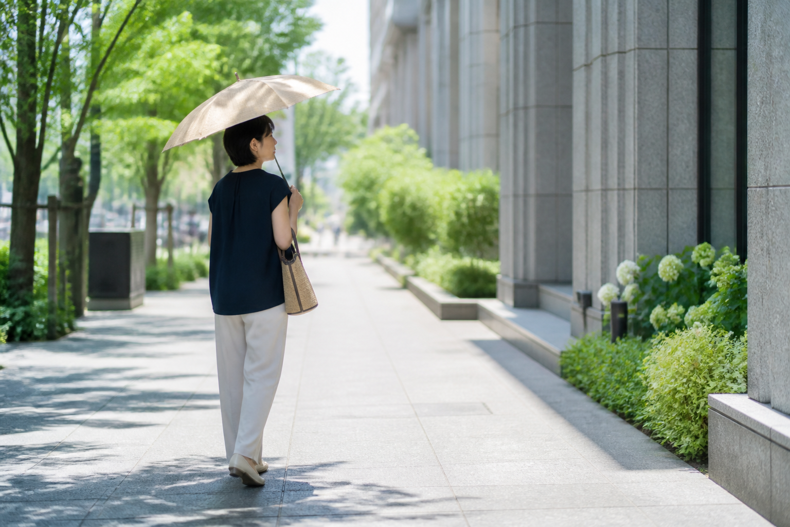 ベージュの晴雨兼用日傘をさして夏の街を歩く女性