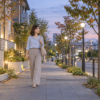秋の夕暮れの明るい歩道を歩く淡いブルーのブラウスの女性